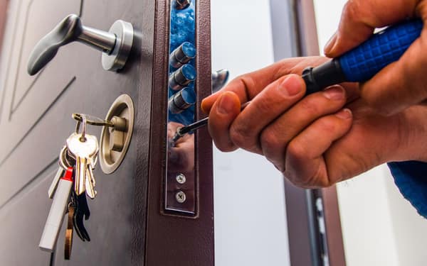 Close-up of hands adjusting the multipoint locking strip on the edge of a security door, keys still in the cylinder.